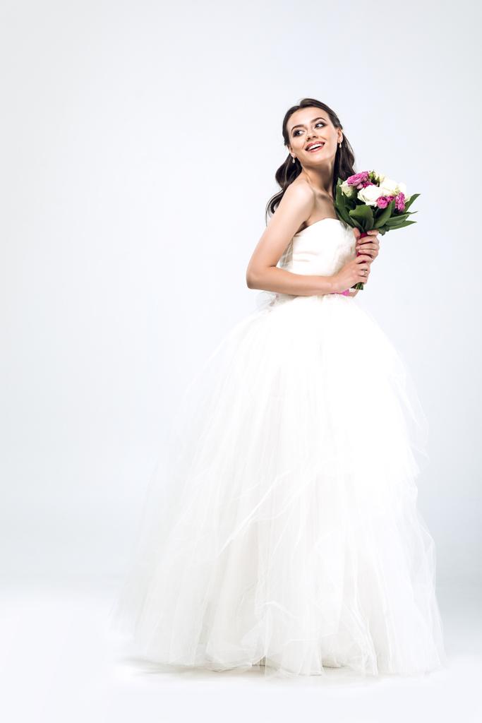schöne junge Braut im Brautkleid mit Blumenstrauß und wegschauen auf weiß - Foto, Bild