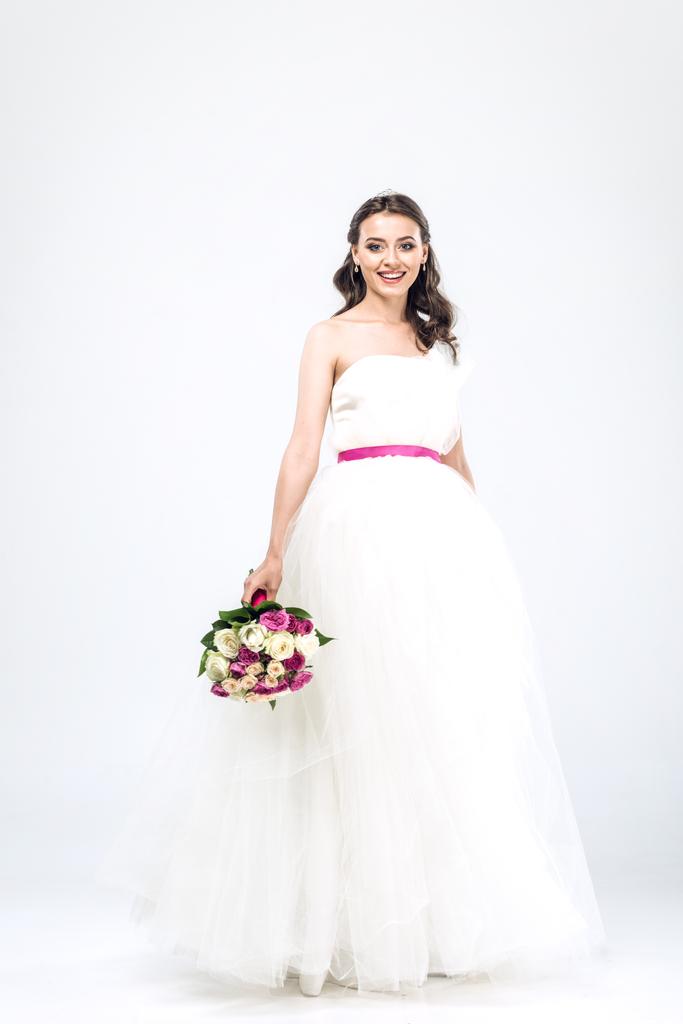 usměvavá mladá nevěsta ve svatebních šatech s kyticí na bílém - Fotografie, Obrázek