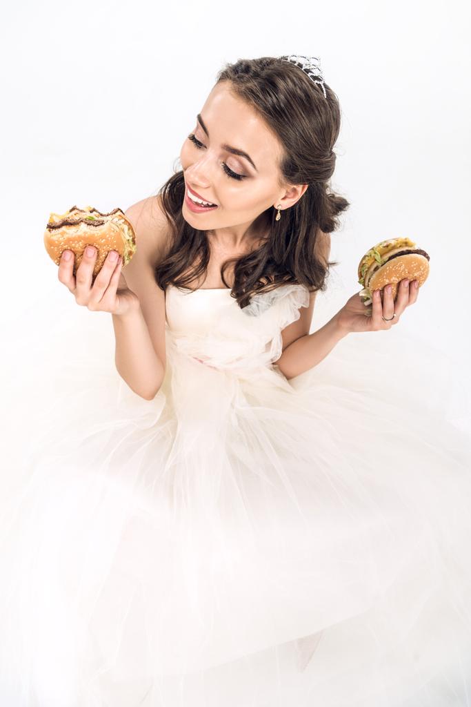 vista de ángulo alto de la novia joven atractiva en vestido de novia con hamburguesas en las manos en blanco
 - Foto, imagen