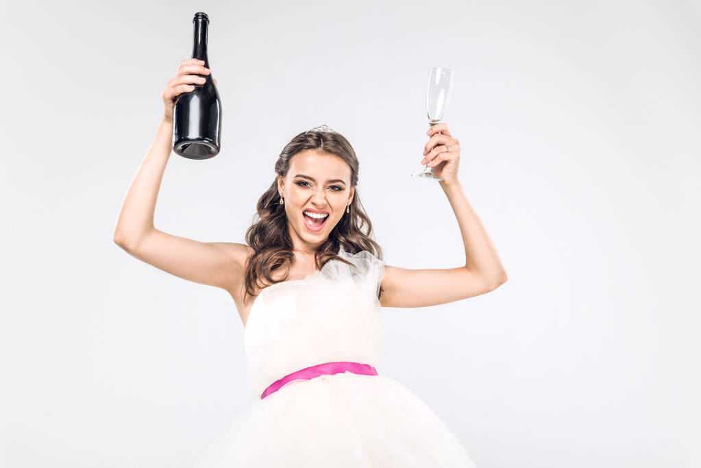feesten van de jonge bruid in trouwjurk met champagne fles en glas geïsoleerd op wit - Foto, afbeelding