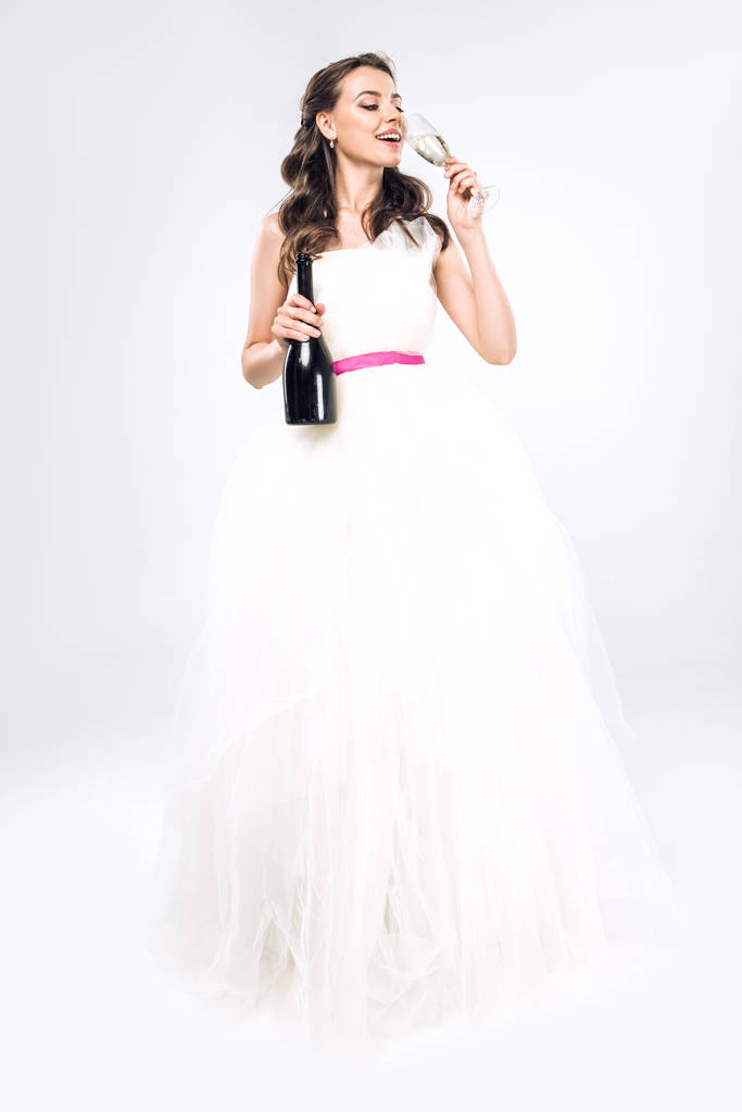 jonge bruid in champagne drinken op witte trouwjurk - Foto, afbeelding
