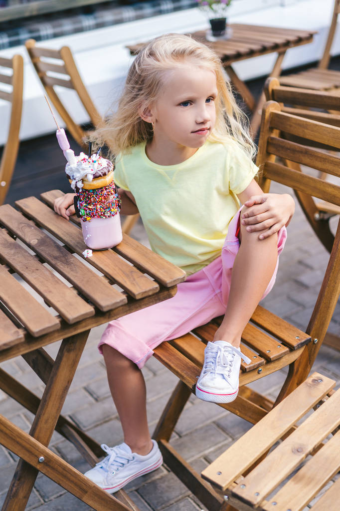 selective focus of little child sitting at table with delicious dessert and looking away in cafe - Photo, Image