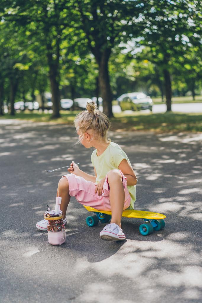 vista lateral da criança sentada no skate na frente da sobremesa na rua
 - Foto, Imagem