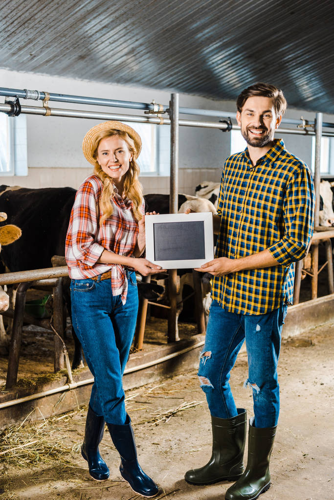 couple of smiling farmers showing blackboard in stable - Photo, Image