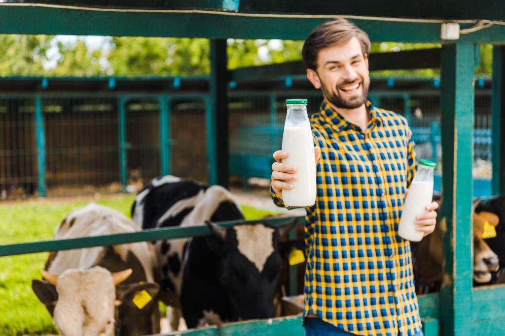 knappe lachende boer tonen van melk van de koe in de buurt van testing - Foto, afbeelding