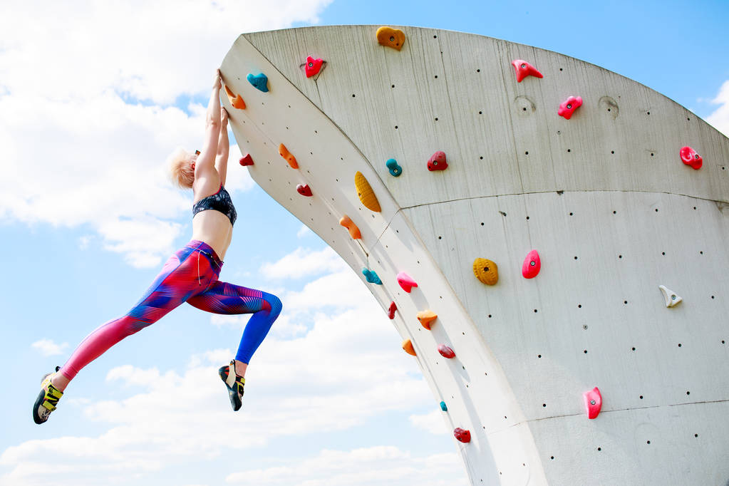 Фото спортивной женщины в леггинсах, висящей на стене для восхождения на голубое небо
 - Фото, изображение