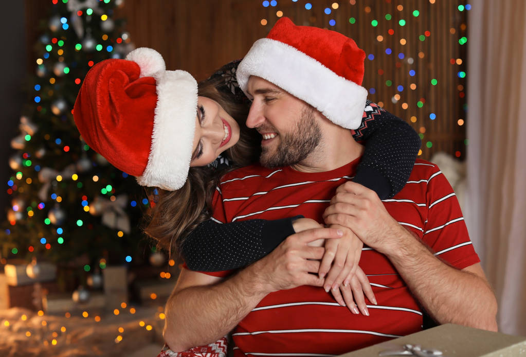 Feliz casal jovem em chapéus de Papai Noel celebrando o Natal em casa
 - Foto, Imagem