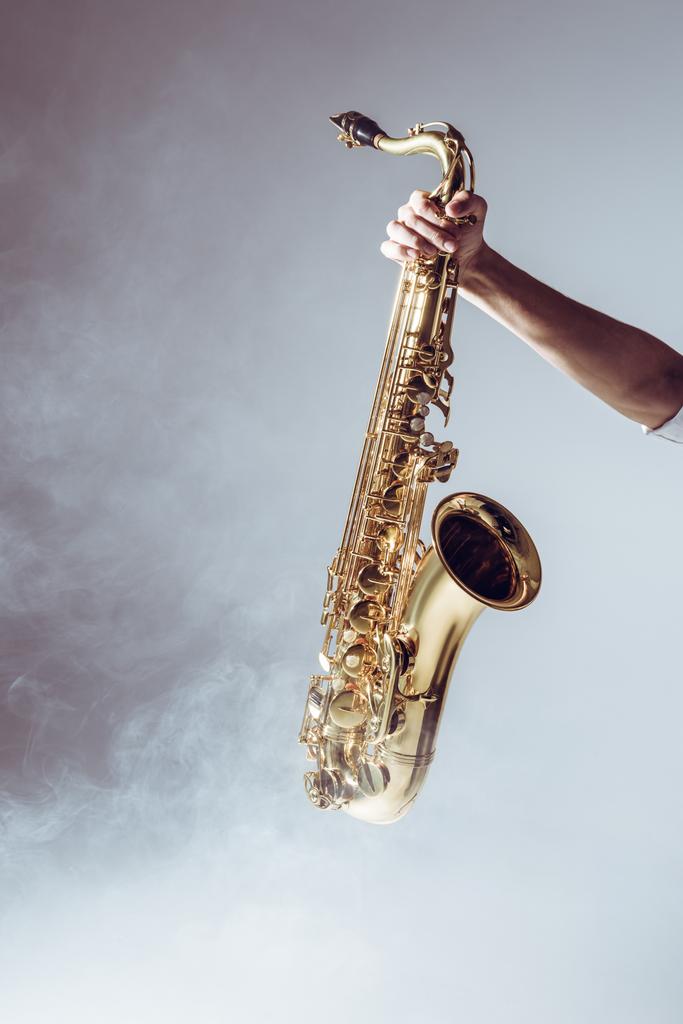 mão no jovem músico segurando saxofone em fumaça no cinza
 - Foto, Imagem