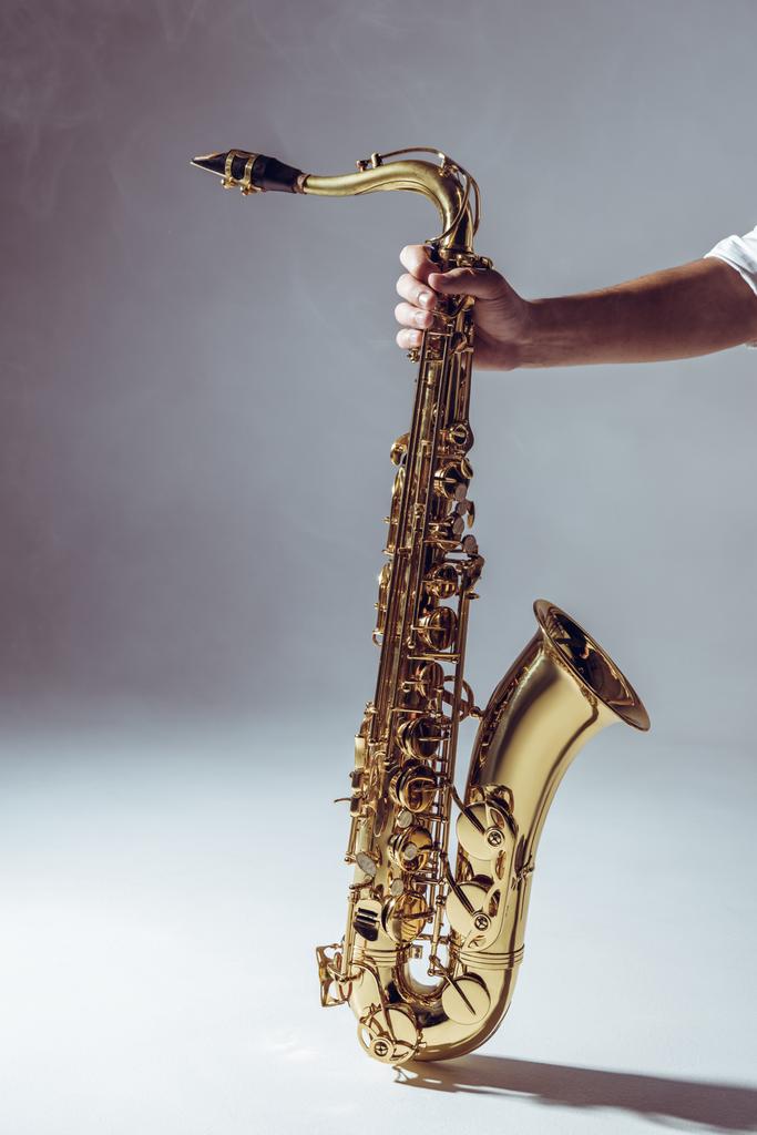 Close-up gedeeltelijke weergave van man met saxofoon in rook op grijs - Foto, afbeelding