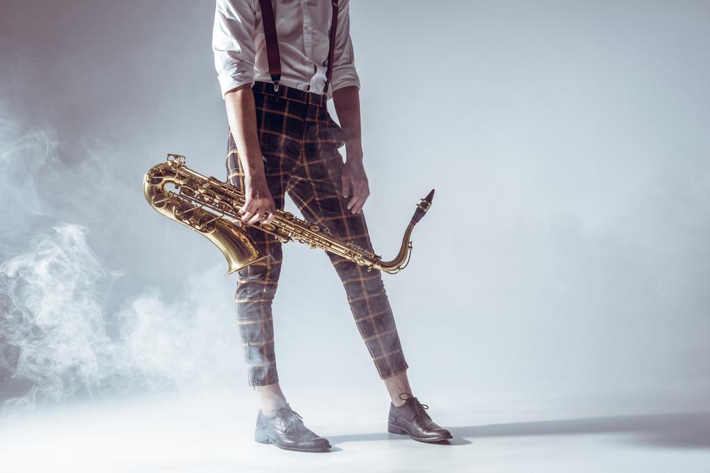 ritagliato colpo di elegante giovane musicista in piedi con sassofono in fumo su grigio
   - Foto, immagini
