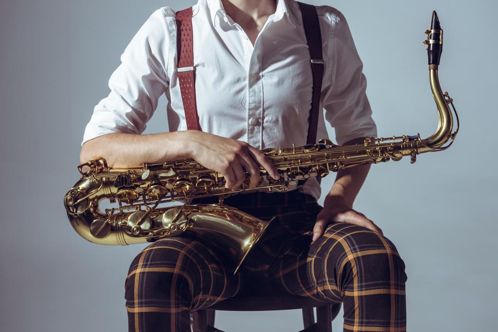 oříznuté záběr mladého hudebníka sedí na židli a drží saxofon izolované Grey - Fotografie, Obrázek