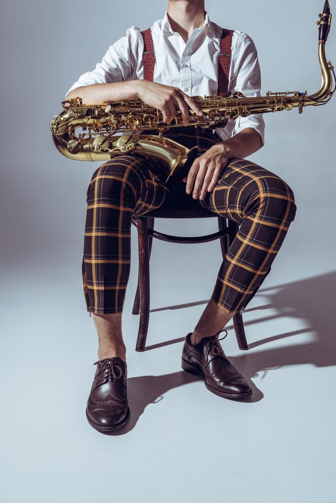 cropped shot of stylish professional musician sitting with saxophone on grey - Photo, Image