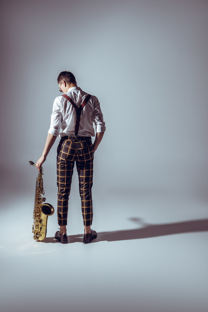 elegáns fiatal zenész, a szaxofon, a szürke állandó hátulnézete - Fotó, kép