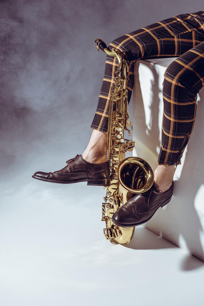 sección baja de músico profesional sentado con saxofón en humo sobre gris
  - Foto, Imagen