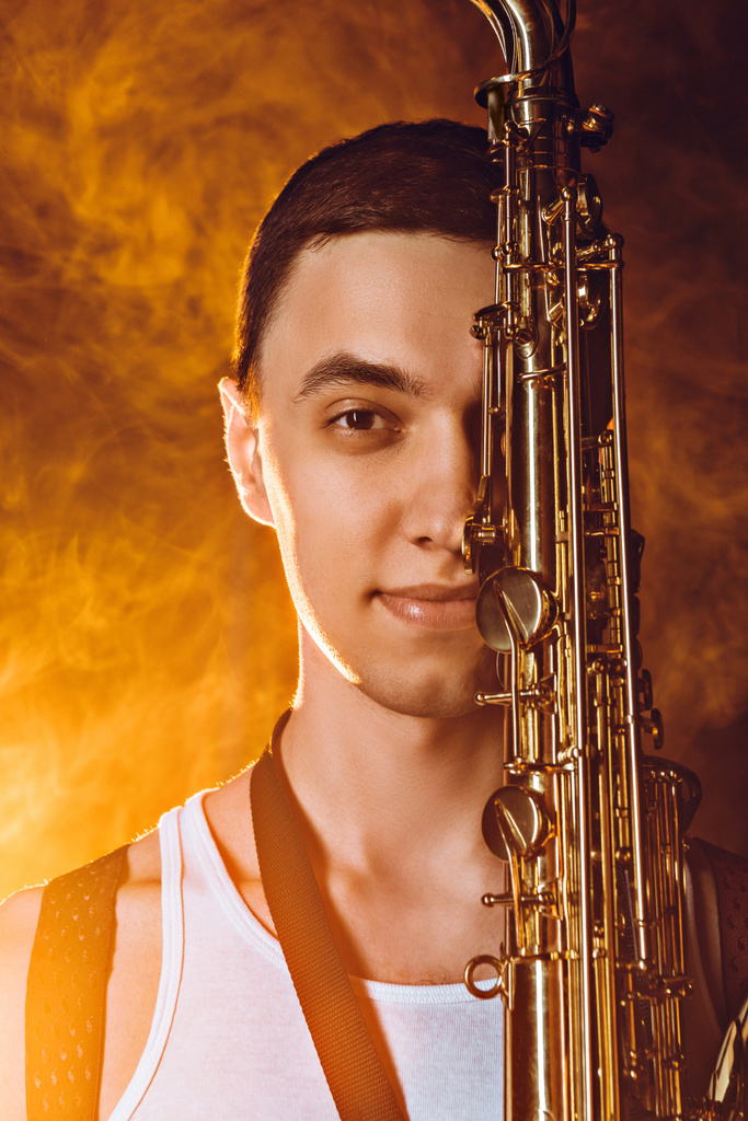 close-up view of handsome young musician with saxophone smiling at camera - Photo, Image