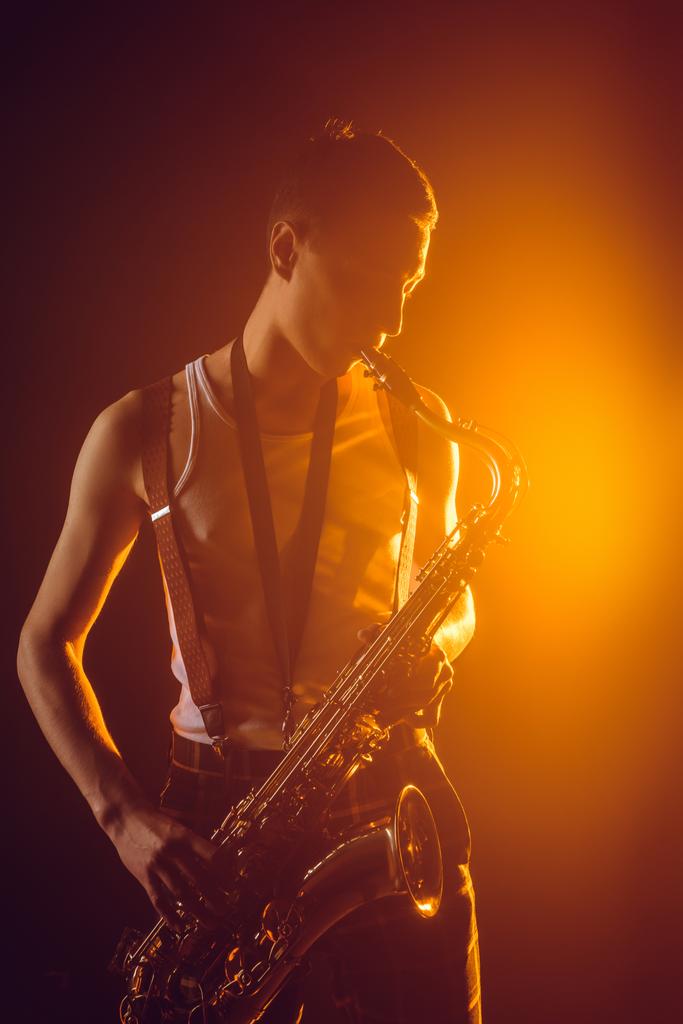 pohledný mladý jazzman saxofon hraje proti reflektor - Fotografie, Obrázek