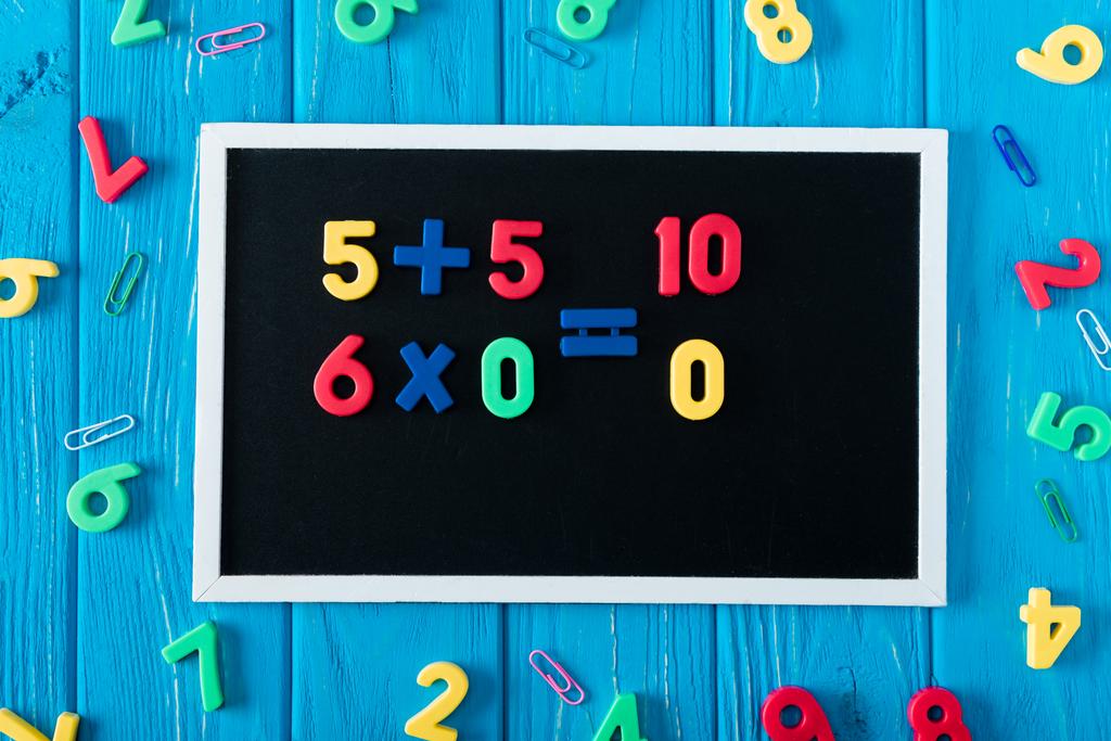 top view of blackboard with math sums, colorful numbers and paper clips on blue wooden background  - Photo, Image