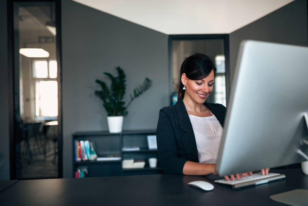 Γυναίκα επιχειρηματίας που εργάζεται ενώ κάθεται σε ένα γραφείο που πληκτρολογείτε στο πληκτρολόγιο του υπολογιστή. - Φωτογραφία, εικόνα