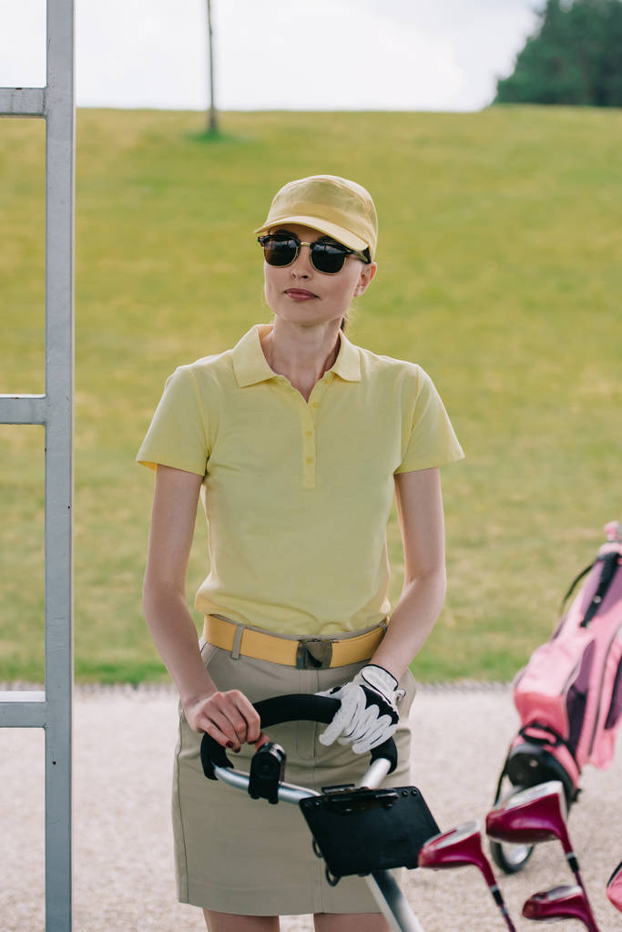 retrato de jugadora de golf en gorra y gafas de sol de pie cerca del equipo de golf en el campo de golf
 - Foto, imagen