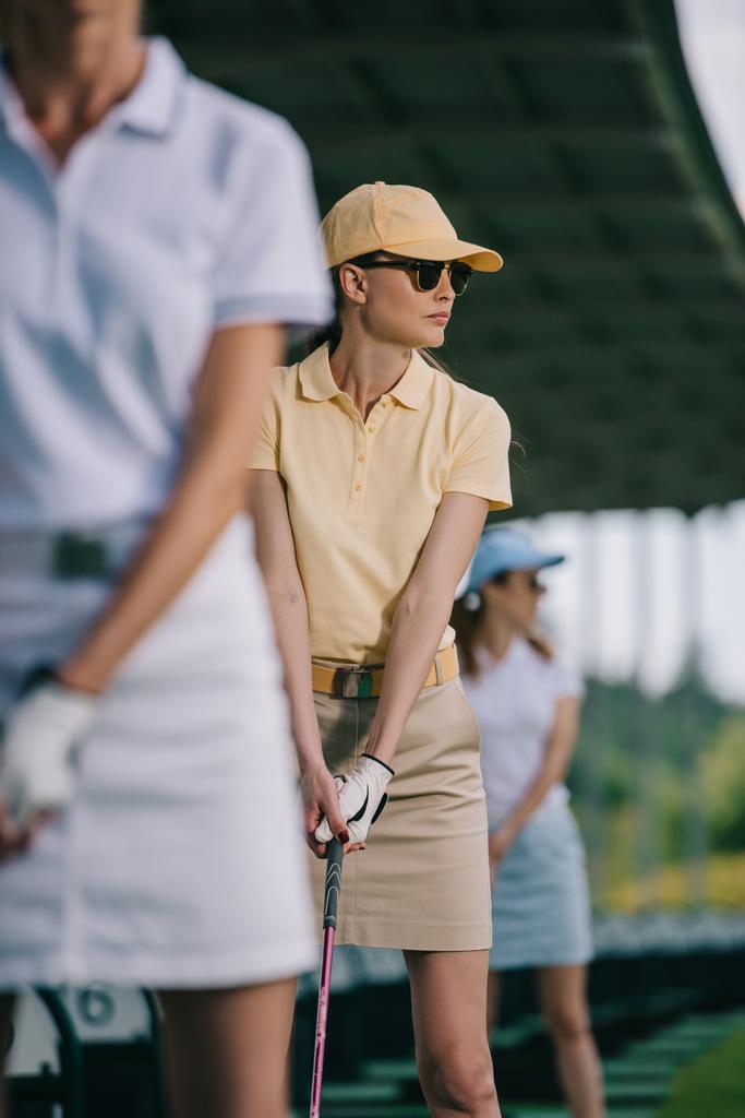Selektywny fokus kobiety w czapkę i okulary przeciwsłoneczne, gry w golfa na polu golfowym - Zdjęcie, obraz