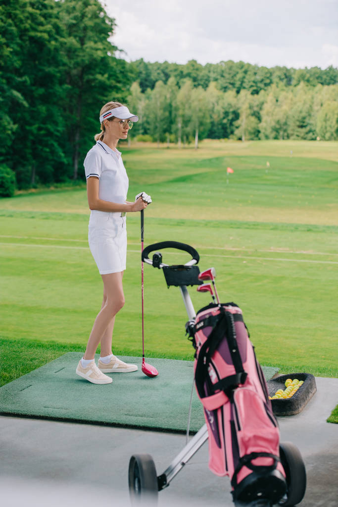 side view of woman in polo and cap with golf club standing at golf course - Photo, Image