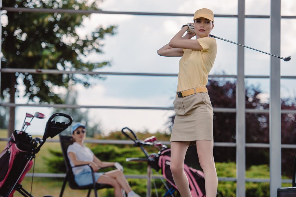 Selektywny fokus kobiet golf gracz gry w golfa, podczas gdy przyjaciel odpoczynku za na polu golfowym - Zdjęcie, obraz