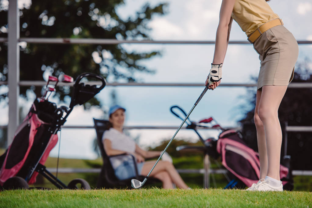 vista parcial de jugador de golf femenino jugando al golf mientras su amigo descansa en el campo de golf
 - Foto, Imagen