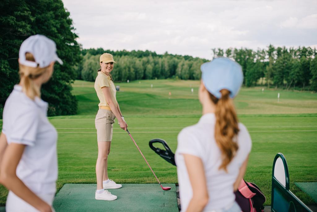 Selektive Fokussierung einer lächelnden Golferin auf Freunde auf dem Golfplatz - Foto, Bild