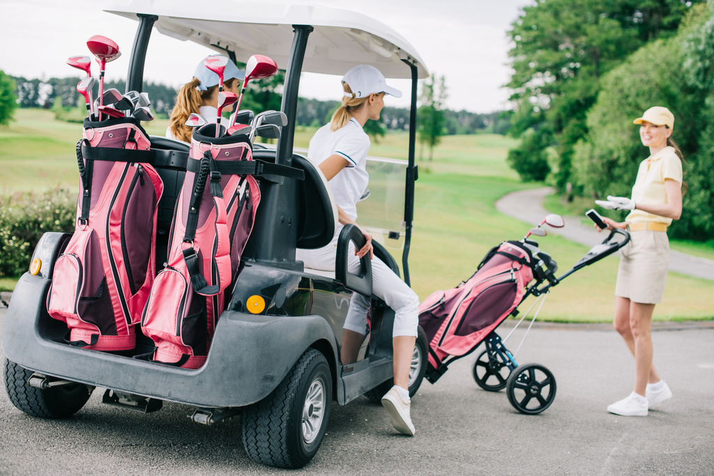 usmívající se ženské golfové hráče na golfový vozík připravuje pro hru na golfovém hřišti - Fotografie, Obrázek