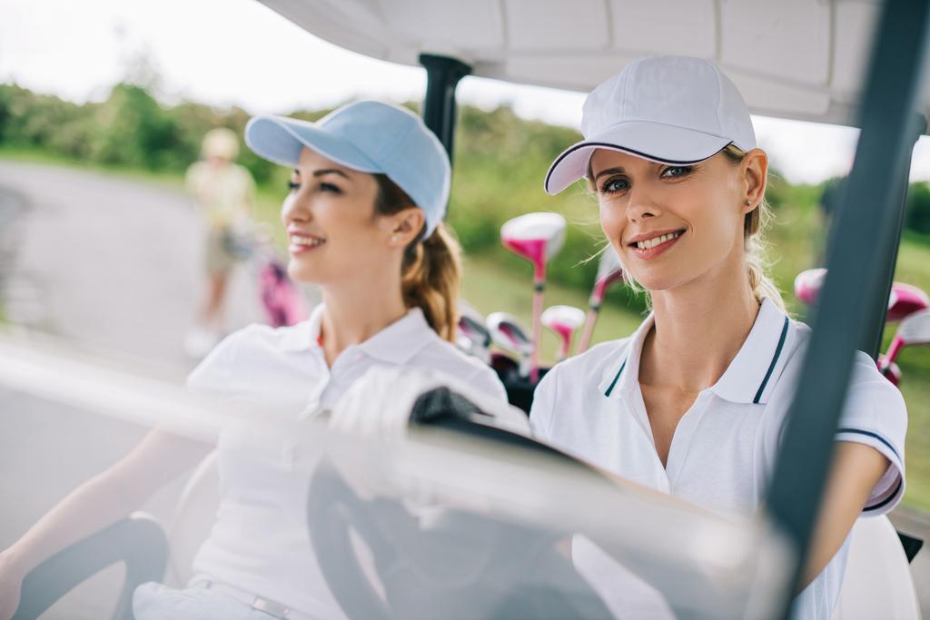 портрет улыбающихся гольфисток в кепках на гольф-каре на поле для гольфа
 - Фото, изображение