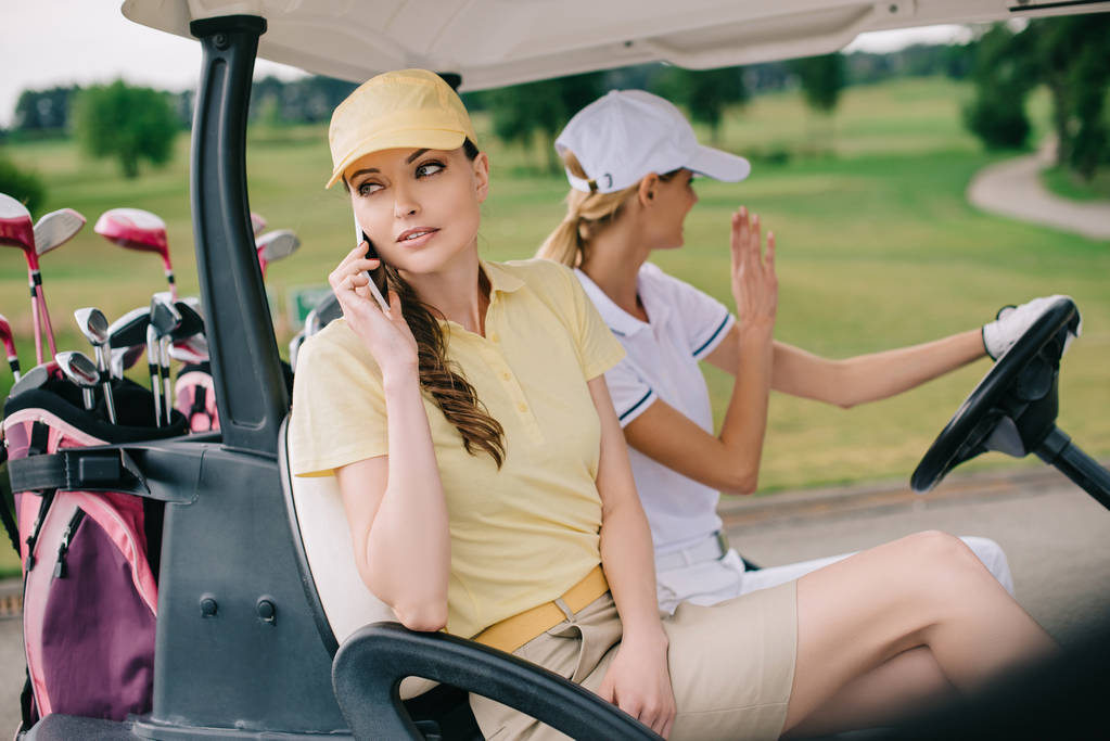 feminino golfista falando no smartphone enquanto montando no carrinho de golfe, juntamente com amigo no campo de golfe
 - Foto, Imagem