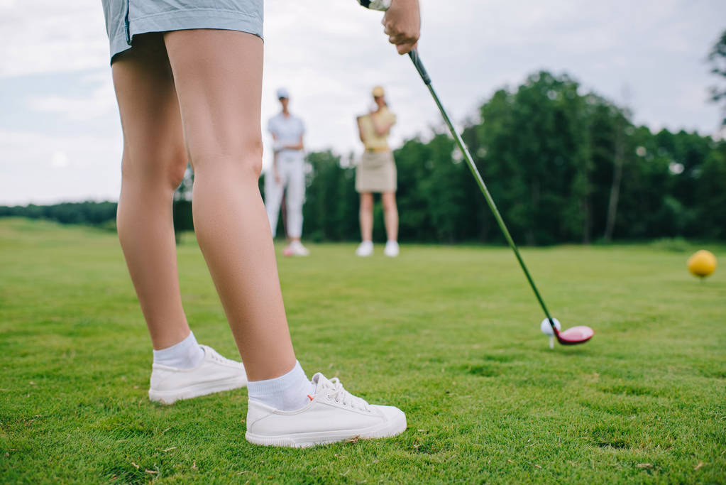 Schnappschuss von Frau beim Golfspielen, während Freunde in der Nähe auf Golfplatz stehen - Foto, Bild