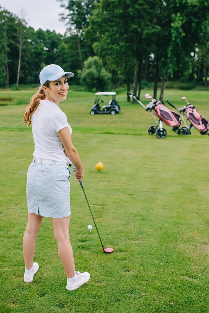 Widok z boku uśmiechnięta kobieta golf gracz w WPR z stoi golf club pole golfowe - Zdjęcie, obraz