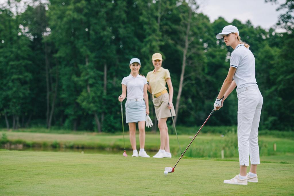 messa a fuoco selettiva della donna in cap giocare a golf mentre gli amici in piedi vicino al campo da golf
 - Foto, immagini