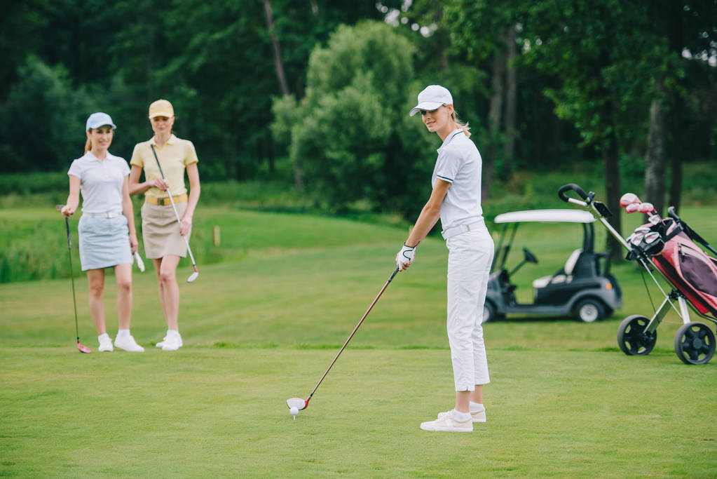 selectieve aandacht van vrouw in GLB golfen terwijl vrienden permanent in de buurt door op golfbaan - Foto, afbeelding