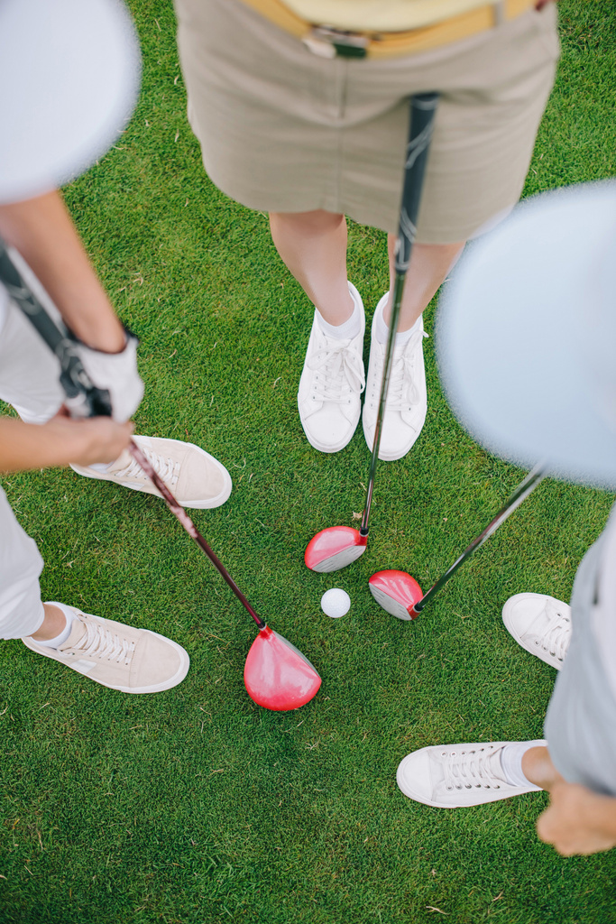 вид зверху жіночих гравців в гольф з гольф-клубами, що стоять на зеленому газоні з м'ячем для гольфу посередині
 - Фото, зображення