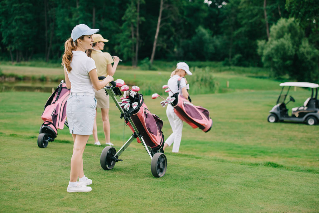 enfoque selectivo de las mujeres con equipo de golf caminando sobre césped verde en el campo de golf
 - Foto, Imagen
