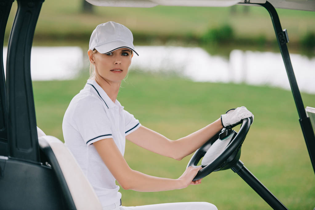 side view of woman in cap and polo riding golf cart at golf course - Photo, Image