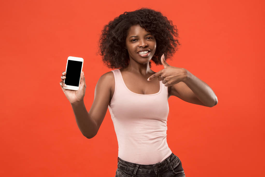Porträt einer selbstbewussten lässigen Afro-Mädchen zeigt leeren Bildschirm Handy isoliert über rotem Hintergrund - Foto, Bild