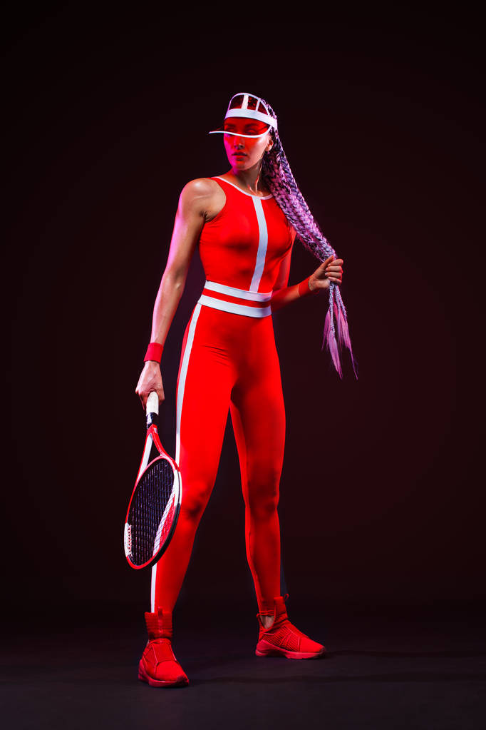 Joueur de tennis. Belle athlète femme avec raquette en costume rouge et chapeau isolé sur fond noir. Concept mode et sport
. - Photo, image