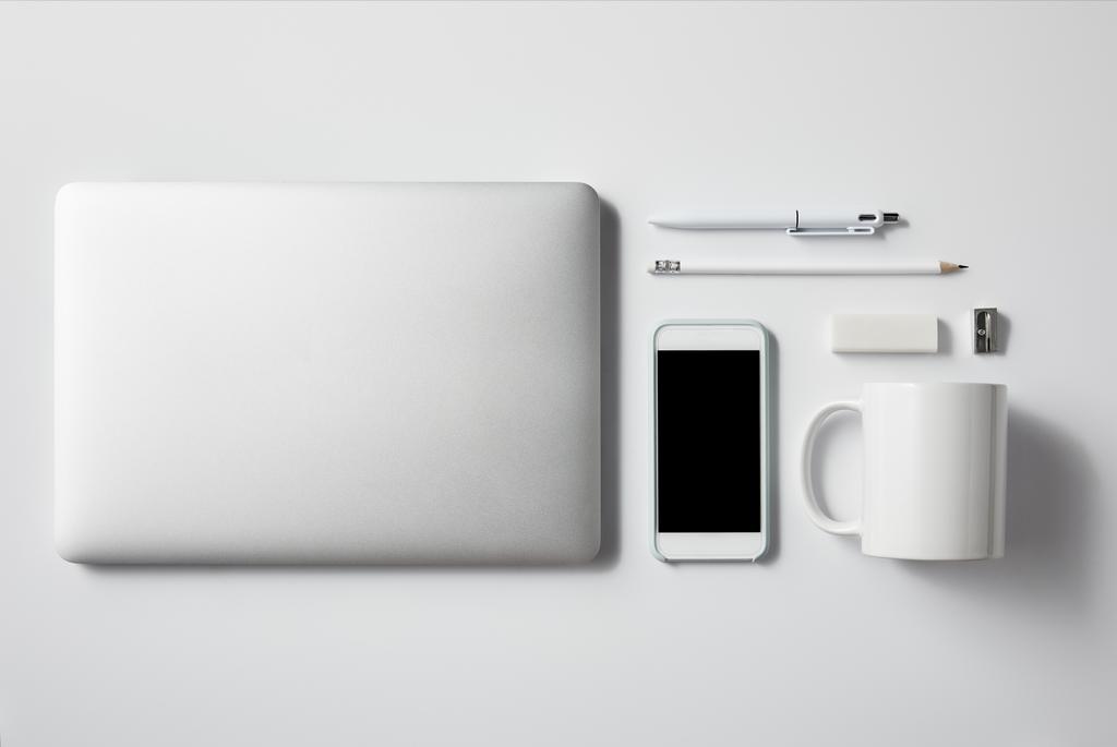 Ansicht von Laptop mit Smartphone und Bürozubehör auf weißer Tischplatte für Attrappen - Foto, Bild