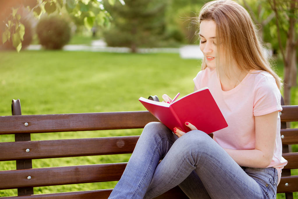  κορίτσι με ένα σημειωματάριο που κάθεται σε ένα παγκάκι στο πάρκο - Φωτογραφία, εικόνα