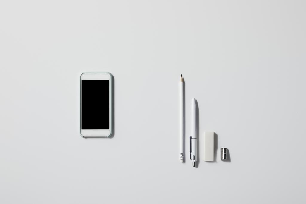 вид зверху смартфона з різними приладдям поспіль на білому столі для маскування
 - Фото, зображення