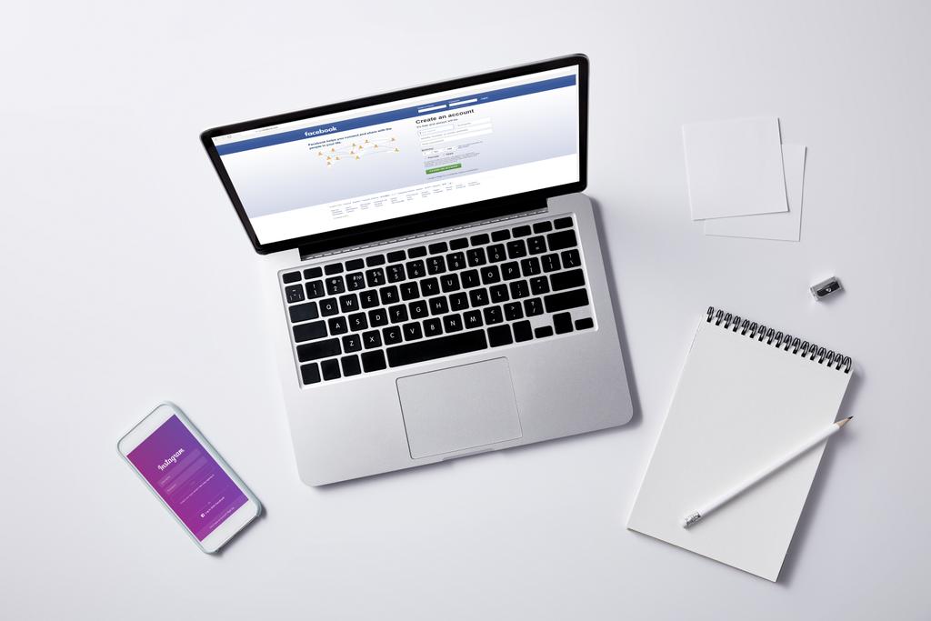 Ansicht von Laptop mit Facebook-Website auf dem Bildschirm und Smartphone mit Instagram-App auf weißer Tischplatte - Foto, Bild