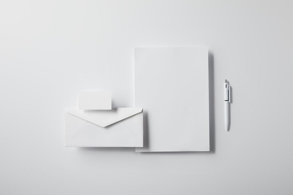 верхний вид конверта с ручкой, пустой бумагой и визитной карточкой на белом столе для макета
 - Фото, изображение