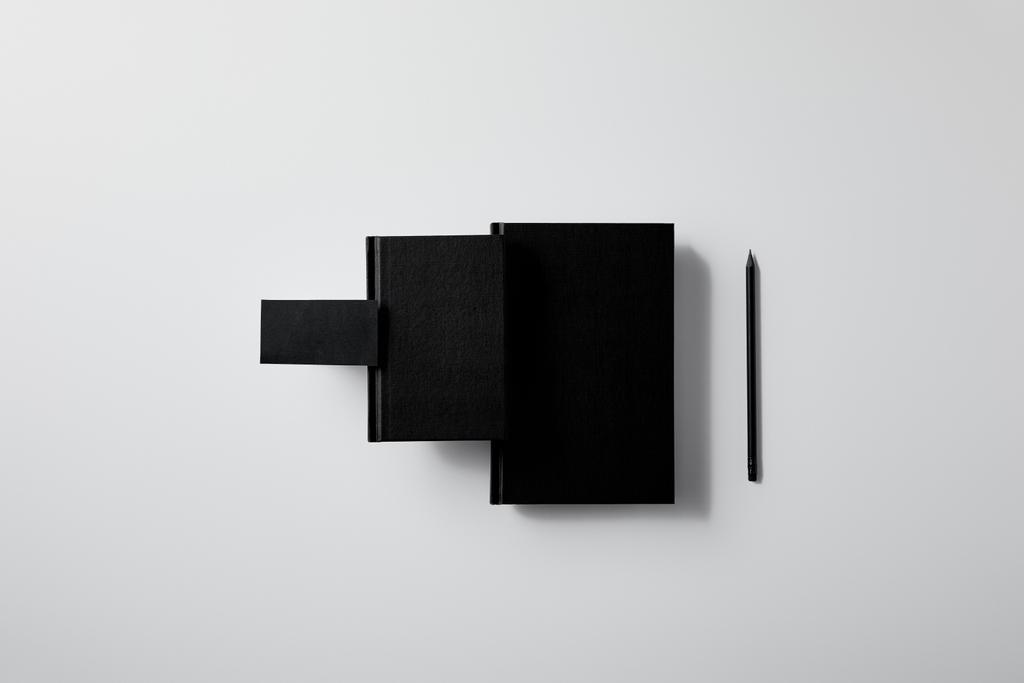 vista superior de cuadernos negros con tarjeta de visita y lápiz en fila en la superficie blanca para maqueta
 - Foto, Imagen