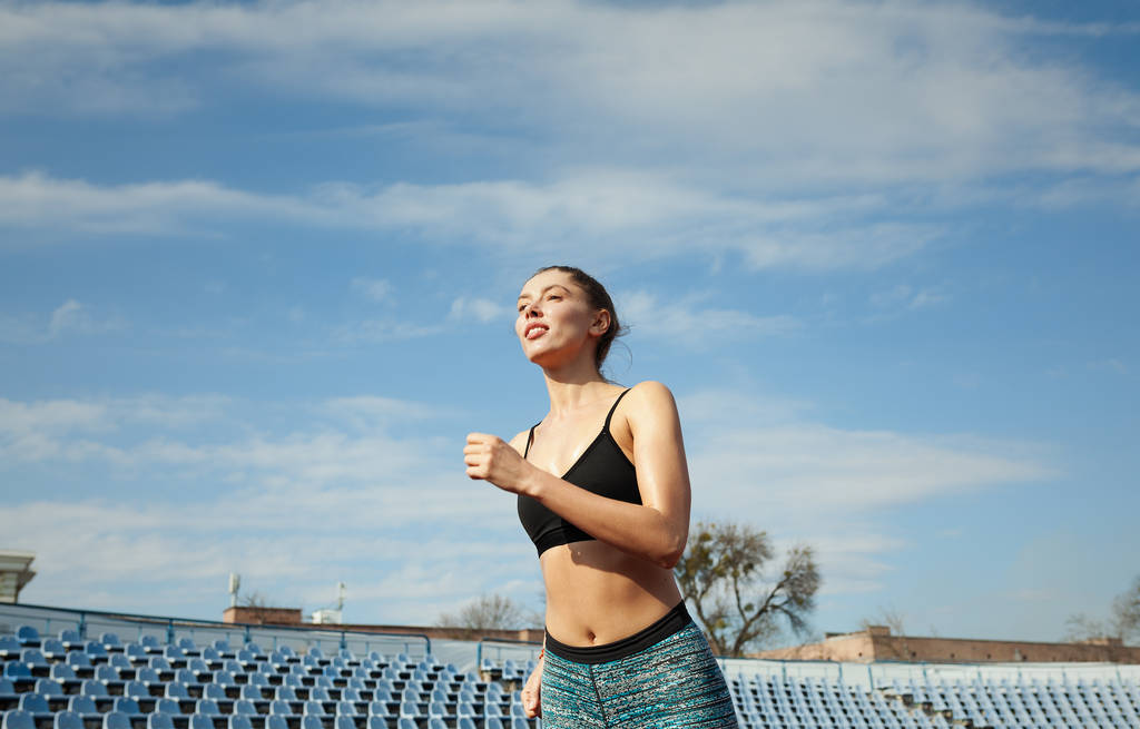 Kaunis nuori sekarotuinen tyttö juoksee juoksumatolla stadionilla. Käsite terveiden elämäntapojen ja laihdutus
 - Valokuva, kuva