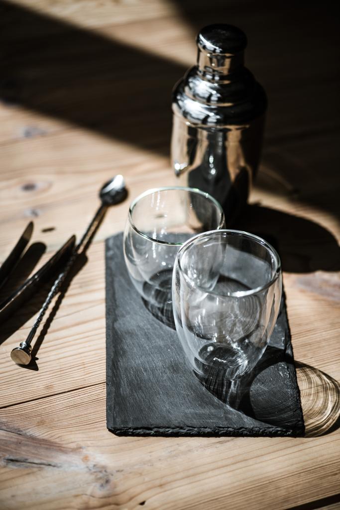 vista close-up de óculos vazios na placa de ardósia, agitador e pinças na mesa de madeira
  - Foto, Imagem