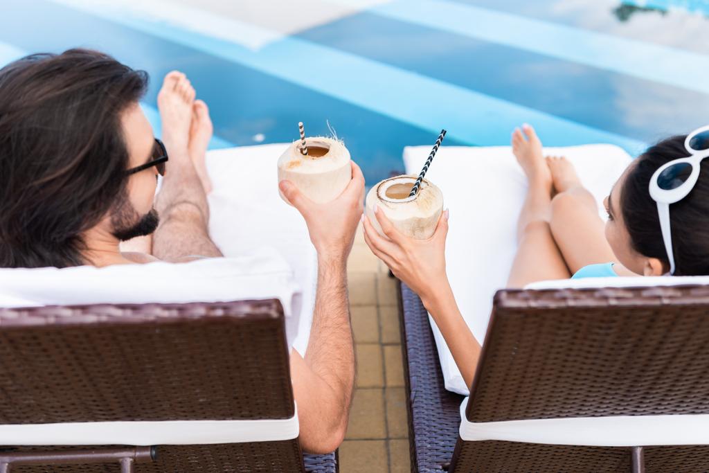 yleisnäkymä pari rentouttava aurinkotuoleja ja clking kookospähkinä cocktaileja
 - Valokuva, kuva