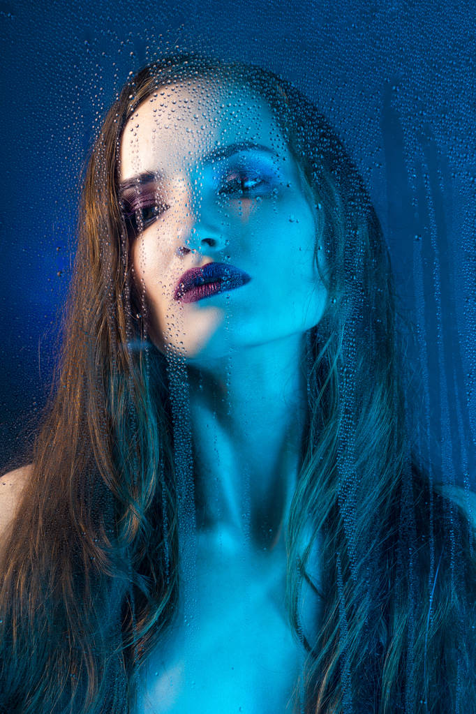 Portret styl sztuka w odcieniach błękitu samotny piękny model smutne dziewczynki za szybą okna, nad którym deszcz spada w dół. Projekt koncepcyjny, komercyjnych i modne. Miejsce. - Zdjęcie, obraz